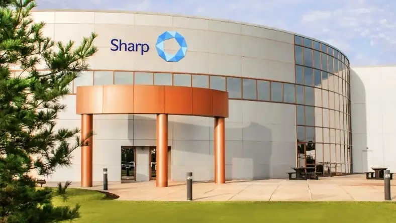 Sharp branded building exterior with curved glass facade and orange entrance columns surrounded by green lawn